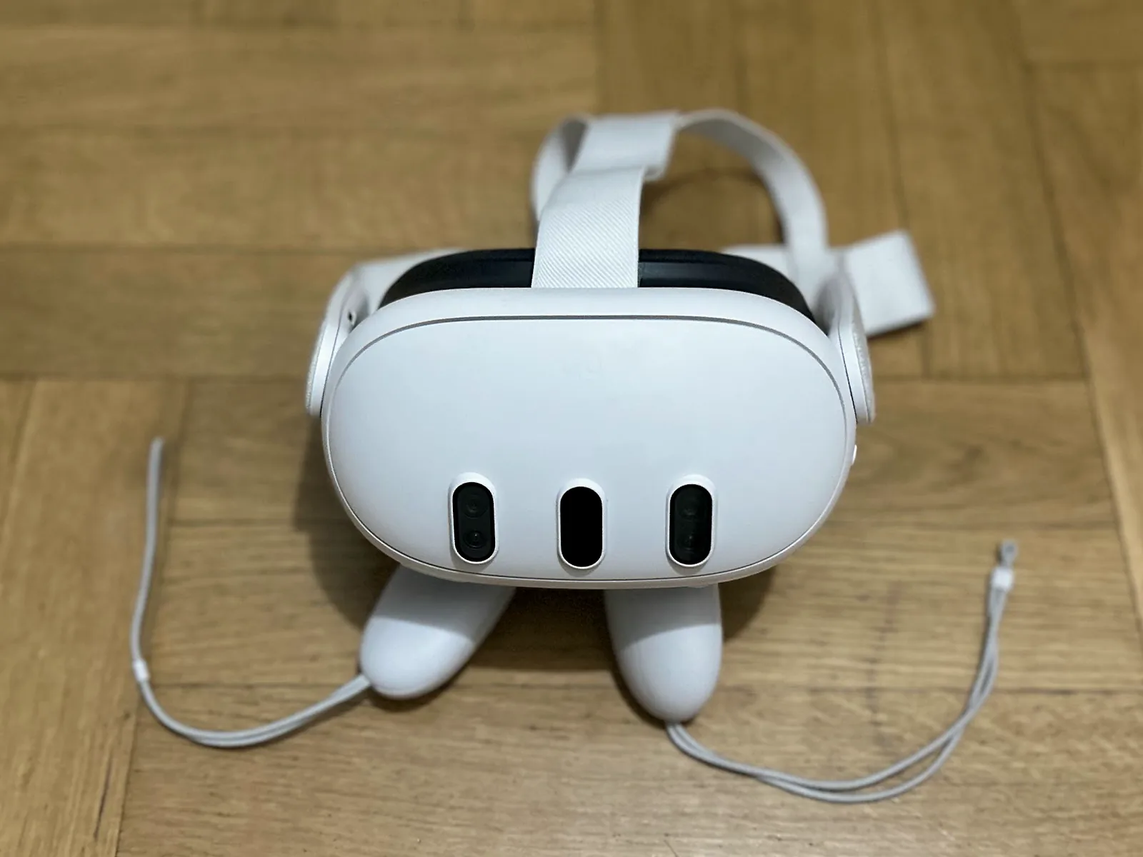 Meta Quest 3 headset resting over its controllers on a wooden floor.