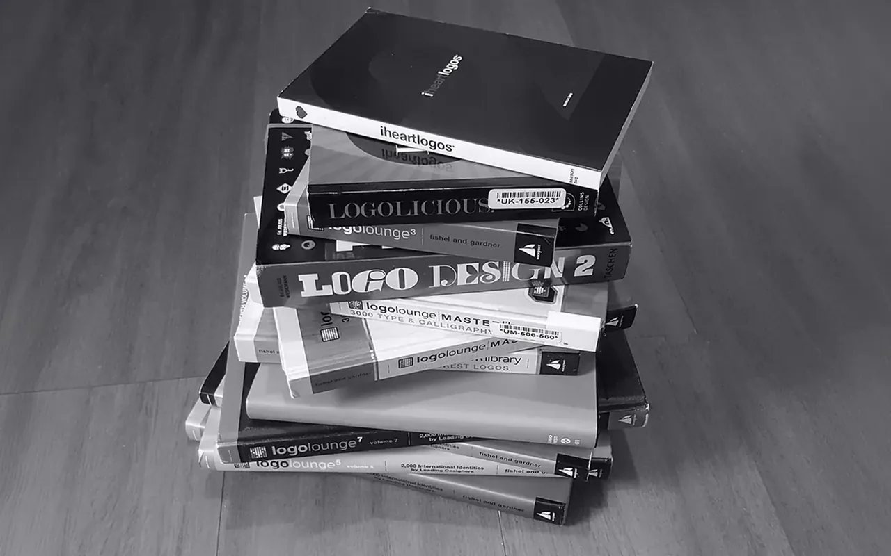 Stack of printed design annuals that feature marks from the studio, including TASCHEN&rsquo;s Logo Design 2 and several LogoLounge volumes